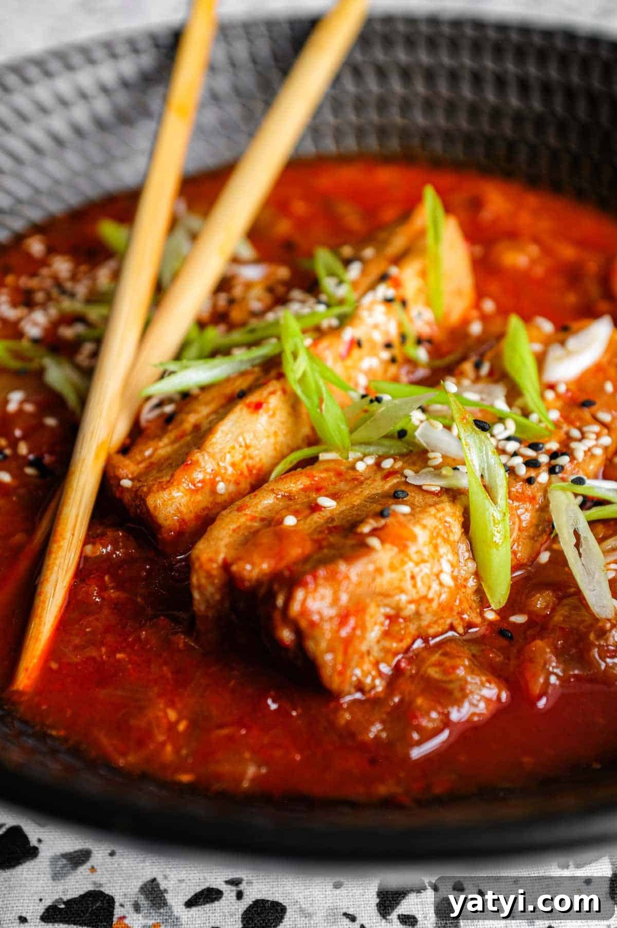 Kimchi Pork Stew | cookeatworld.com A large black bowl of Kimchi Pork Stew scattered with sesame seeds, nigella seeds and spring onion with chopsticks on the side.