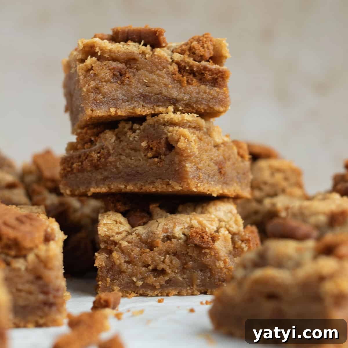 a stack of 3 biscoff blondies with other blondies scattered around them