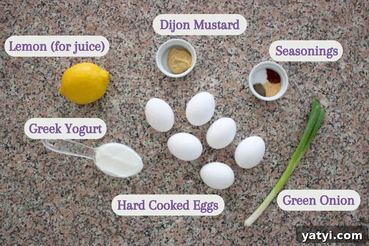Creamy Egg Salad Without Mayo: Tangy Avocado & Yogurt Recipe 3 Ingredients for egg salad, including a lemon, cup of Greek yogurt, five hard-cooked eggs, Dijon mustard, assorted seasonings in a small dish, and a green onion, are arranged on a speckled countertop.