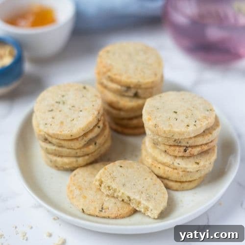 Rosemary Parmesan Shortbread Made with Sourdough Discard 10 Stacked sourdough discard rosemary and parmesan shortbread biscuits on a serving plate with one broken in half to show texture.