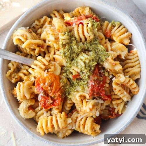 bowl with pesto pasta topped with cherry tomato sauce and more pesto.