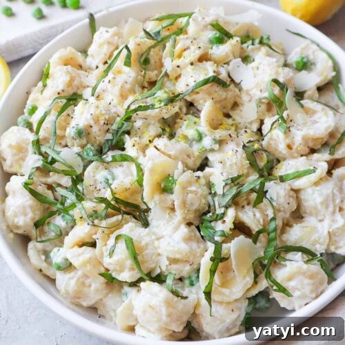 white bowl with ricotta pasta and peas topped with parmesan and basil.