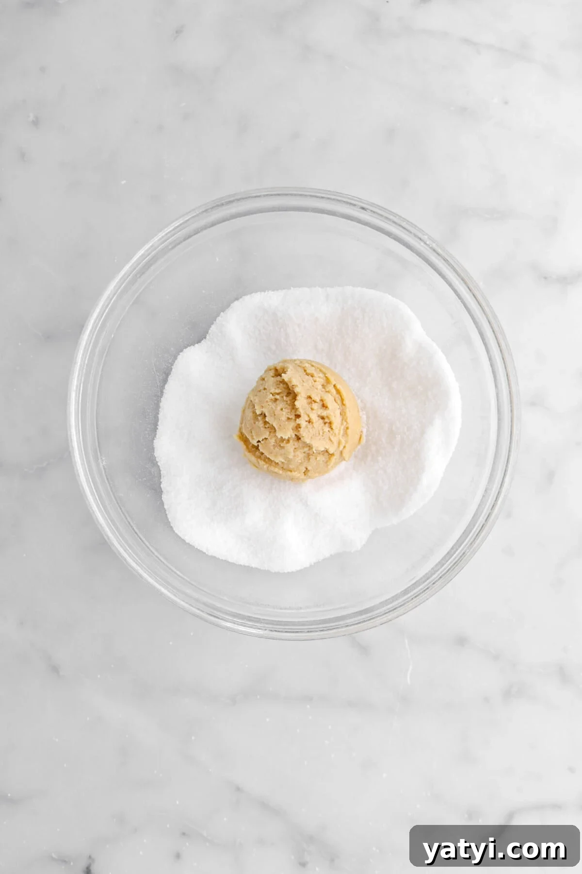 cookie dough ball in bowl of sugar.