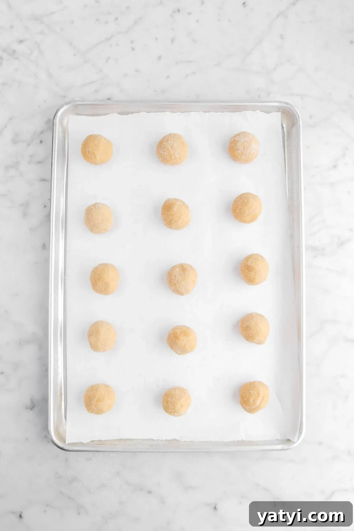 fifteen cookie dough balls on lined sheet pan.