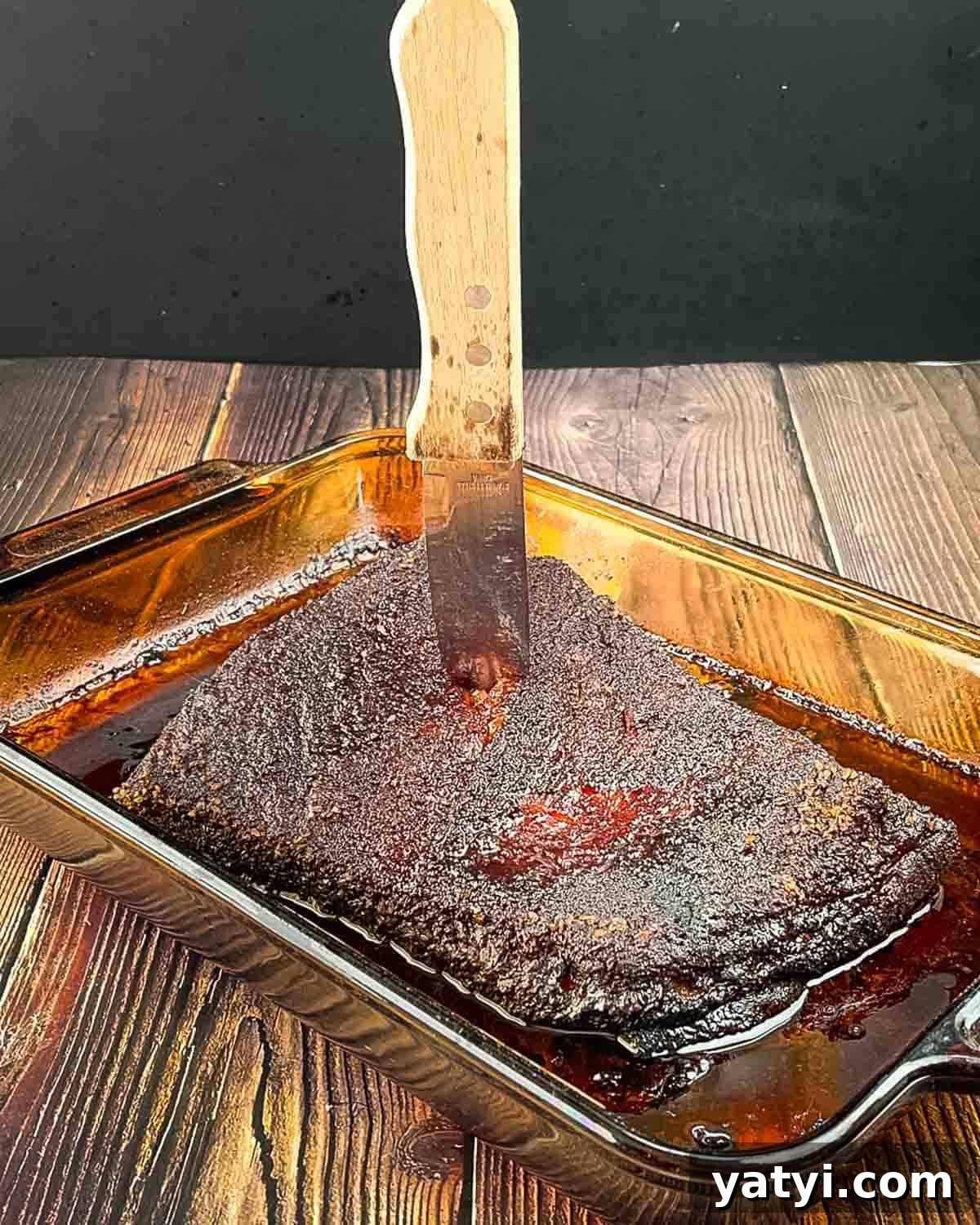 A knife in the brisket touching the bottom of the pan, indicating perfect doneness.