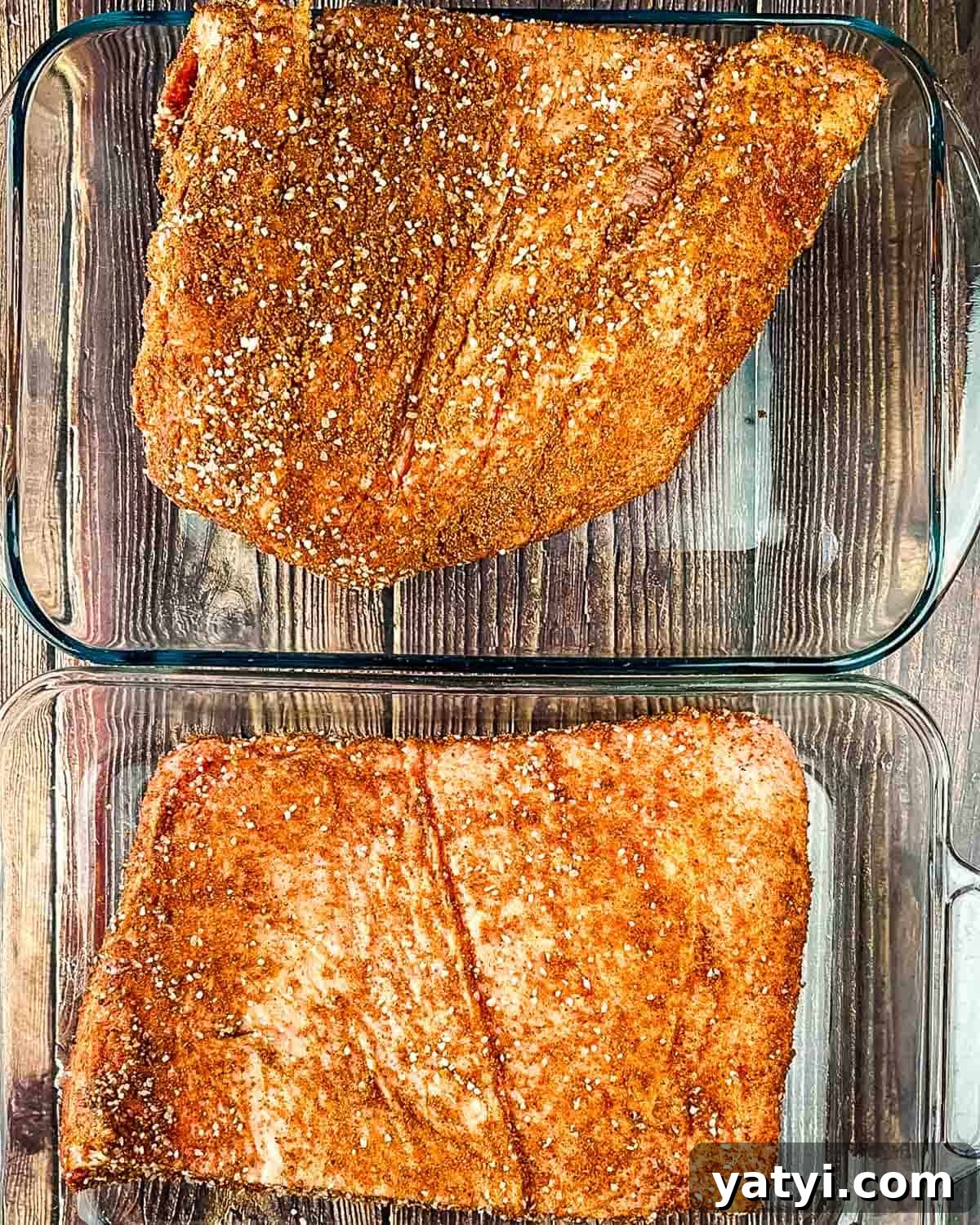 The brisket pieces in a baking pan, covered liberally in dry rub.