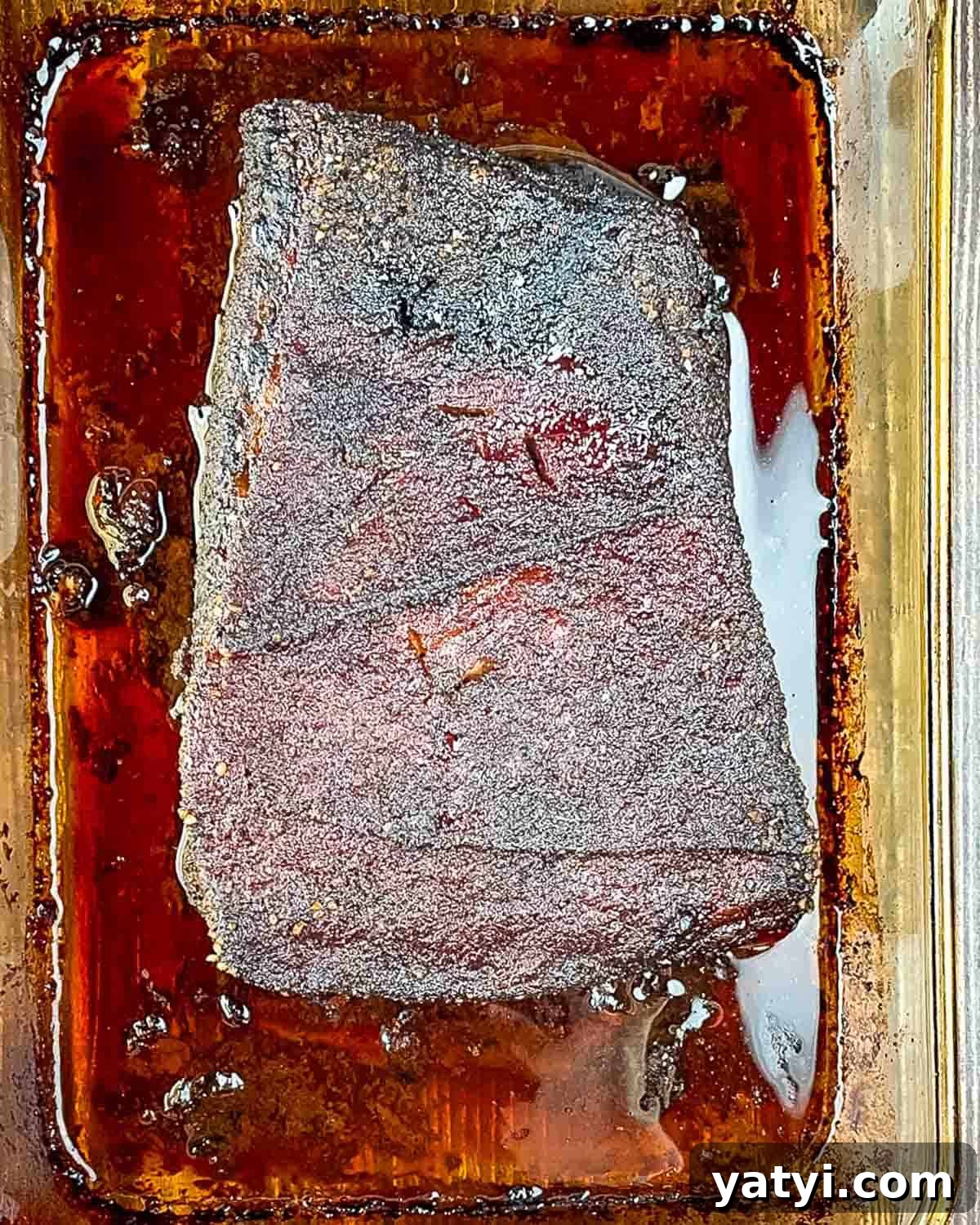 The finished brisket in the baking pan, showing a dark bark. 