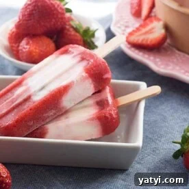 Strawberry pistachio yoghurt popsicles in a small rectangular white dish on a blue background and with strawberries in the background.