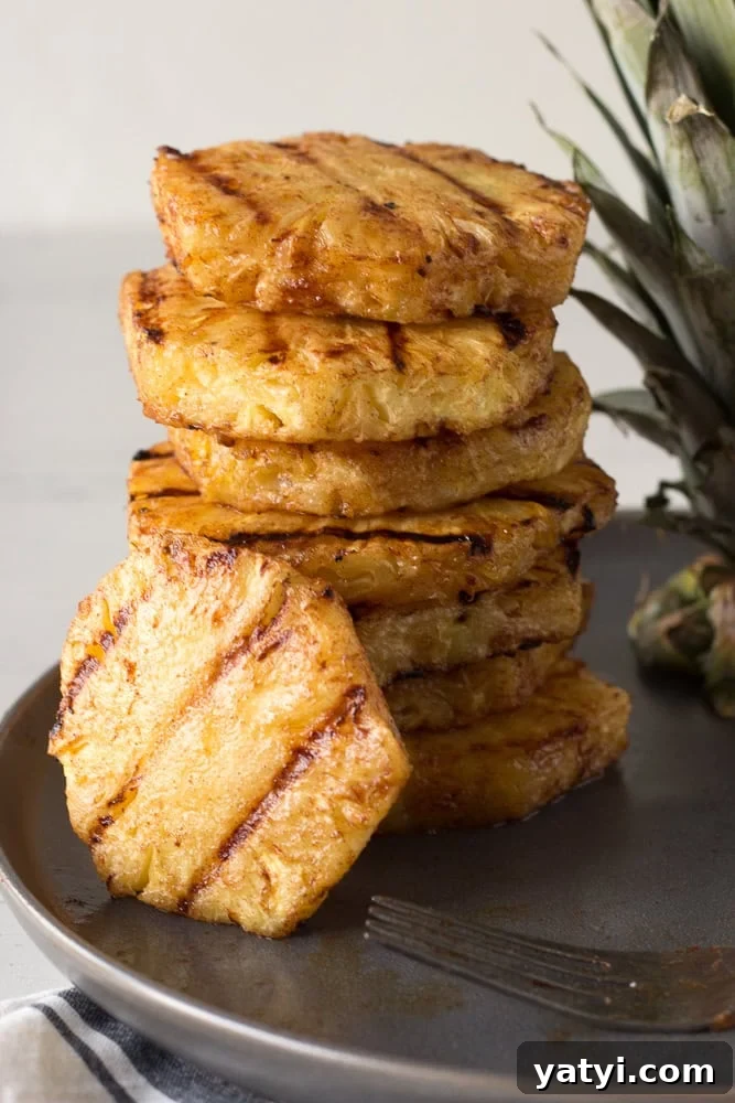 Juicy Grilled Pineapple Recipe — Naturally Sweet, No Added Sugar 11 Grilled pineapple slices stacked on a gray plate with one slice leaning to the side.