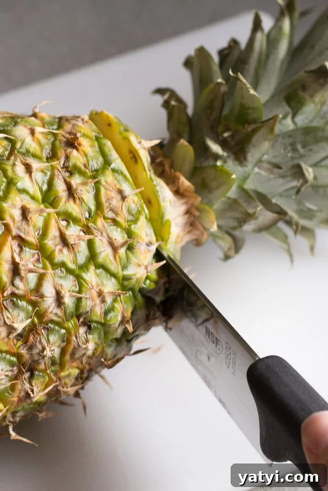 Juicy Grilled Pineapple Recipe — Naturally Sweet, No Added Sugar 3 A sharp knife cutting the top off a pineapple on a white cutting board.