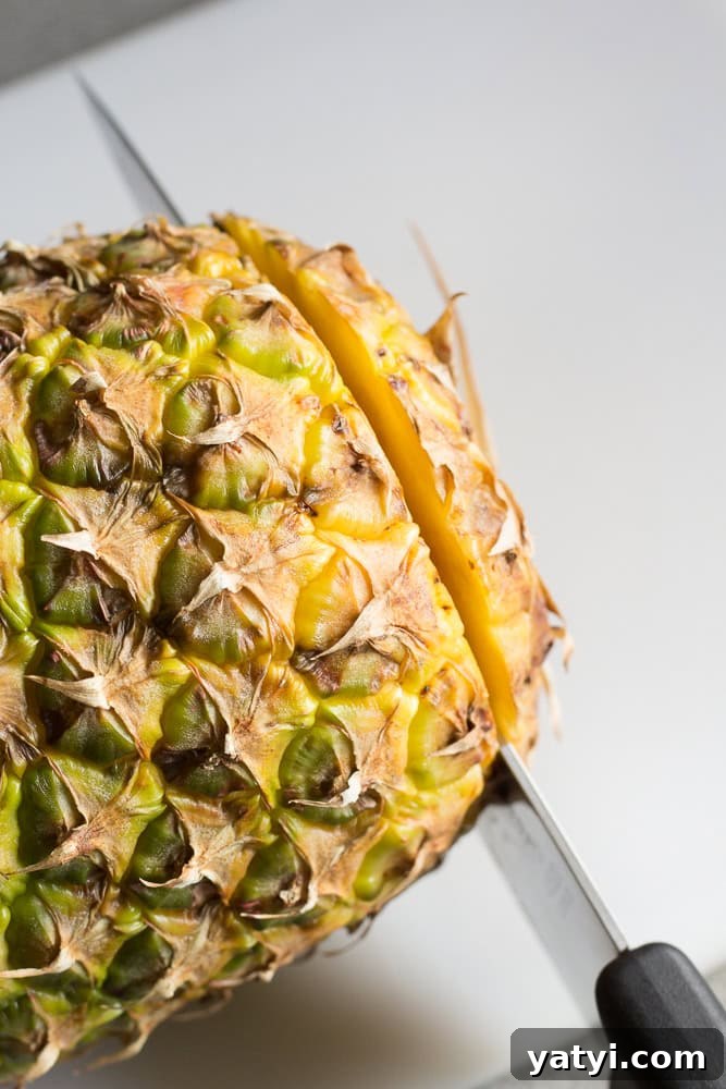 Juicy Grilled Pineapple Recipe — Naturally Sweet, No Added Sugar 4 A large sharp knife cutting the bottom off a pineapple on a white cutting board.
