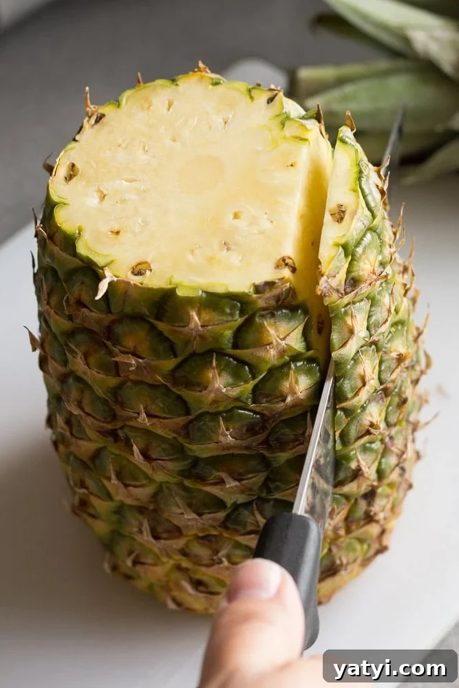 Juicy Grilled Pineapple Recipe — Naturally Sweet, No Added Sugar 5 A large sharp knife cutting the skin off the sides of a pineapple on a white cutting board.