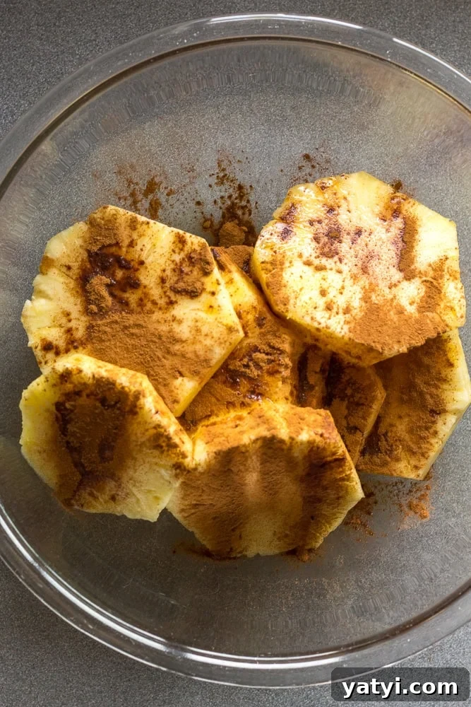 Juicy Grilled Pineapple Recipe — Naturally Sweet, No Added Sugar 8 Slices of pineapple in a large clear bowl with cinnamon sprinkled on top.