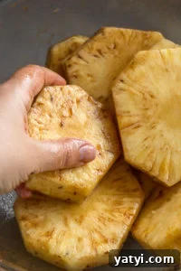 Juicy Grilled Pineapple Recipe — Naturally Sweet, No Added Sugar 9 A hand rubbing in oil and cinnamon onto pineapple slices in a large clear bowl.