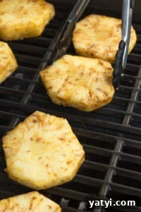 Juicy Grilled Pineapple Recipe — Naturally Sweet, No Added Sugar 10 A pair of tongs placing slices of pineapple on a grill.