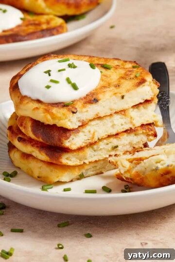 Stack of air fryer potato cakes on a plate with a dollop of sour cream and chopped chives on top.