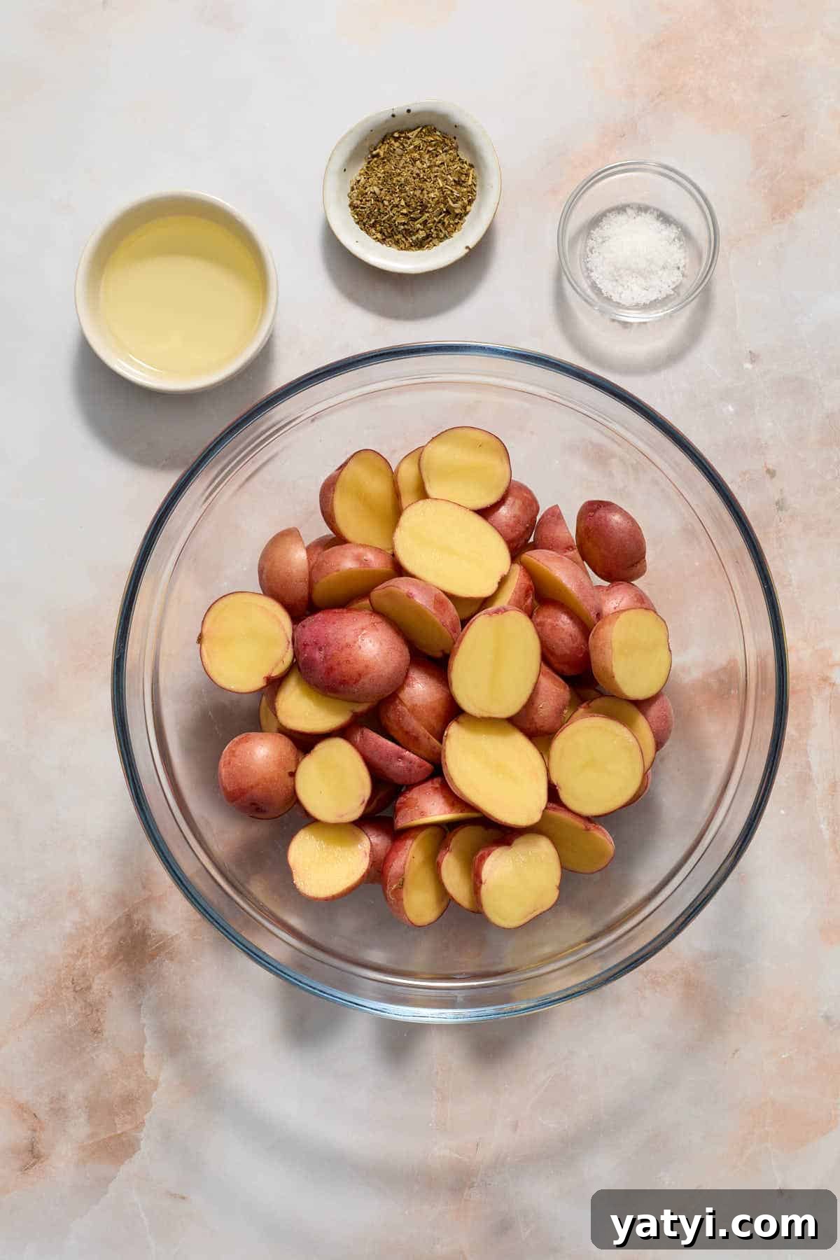 Crispy Air Fryer Baby Potatoes — 4 Ingredients Only 4 Potatoes cut in half and placed in a glass bowl with oil, seasonings and salt on the side.