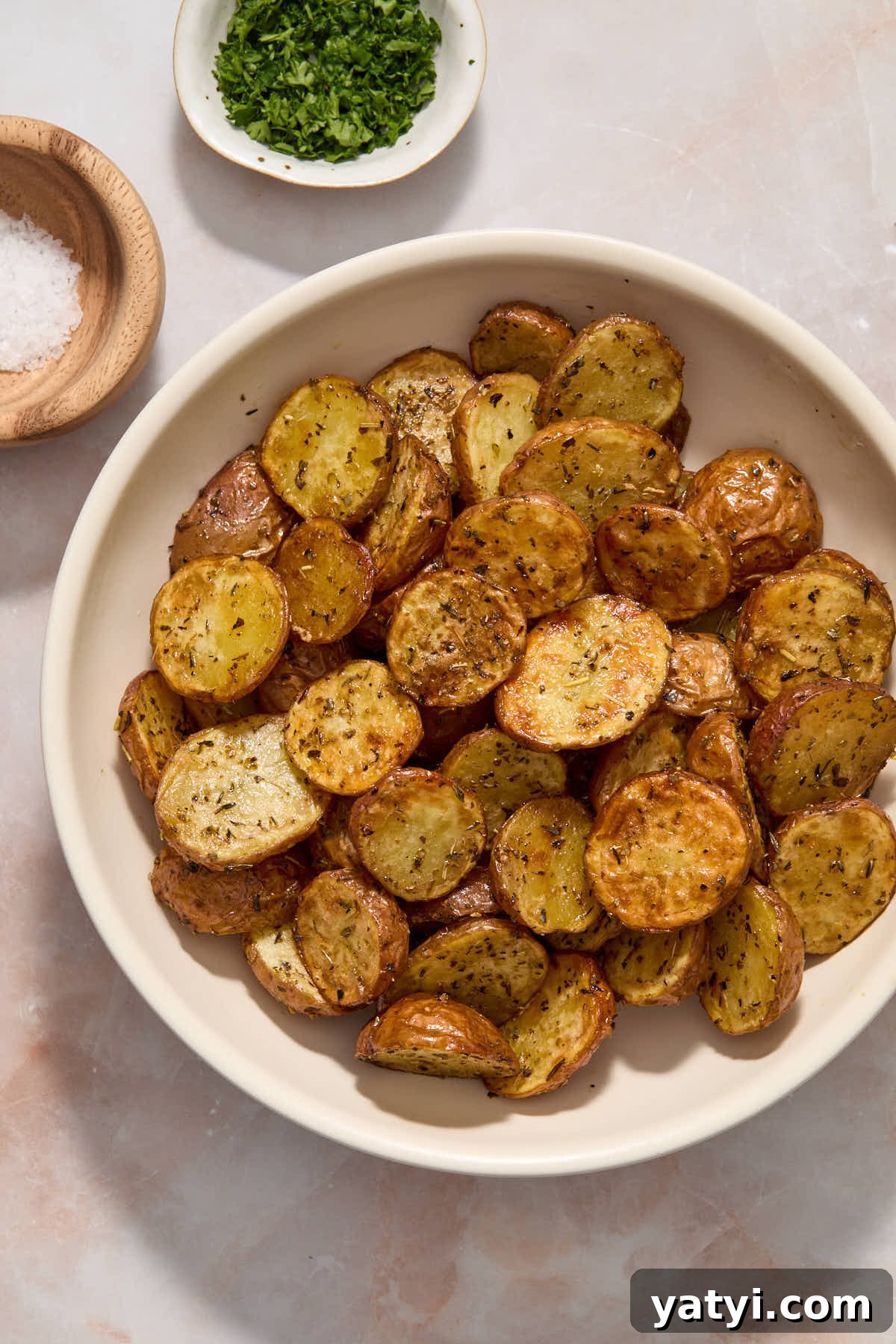 Crispy Air Fryer Baby Potatoes — 4 Ingredients Only 8 Potatoes served in a white bowl with sea salt and chopped parsley on the side.