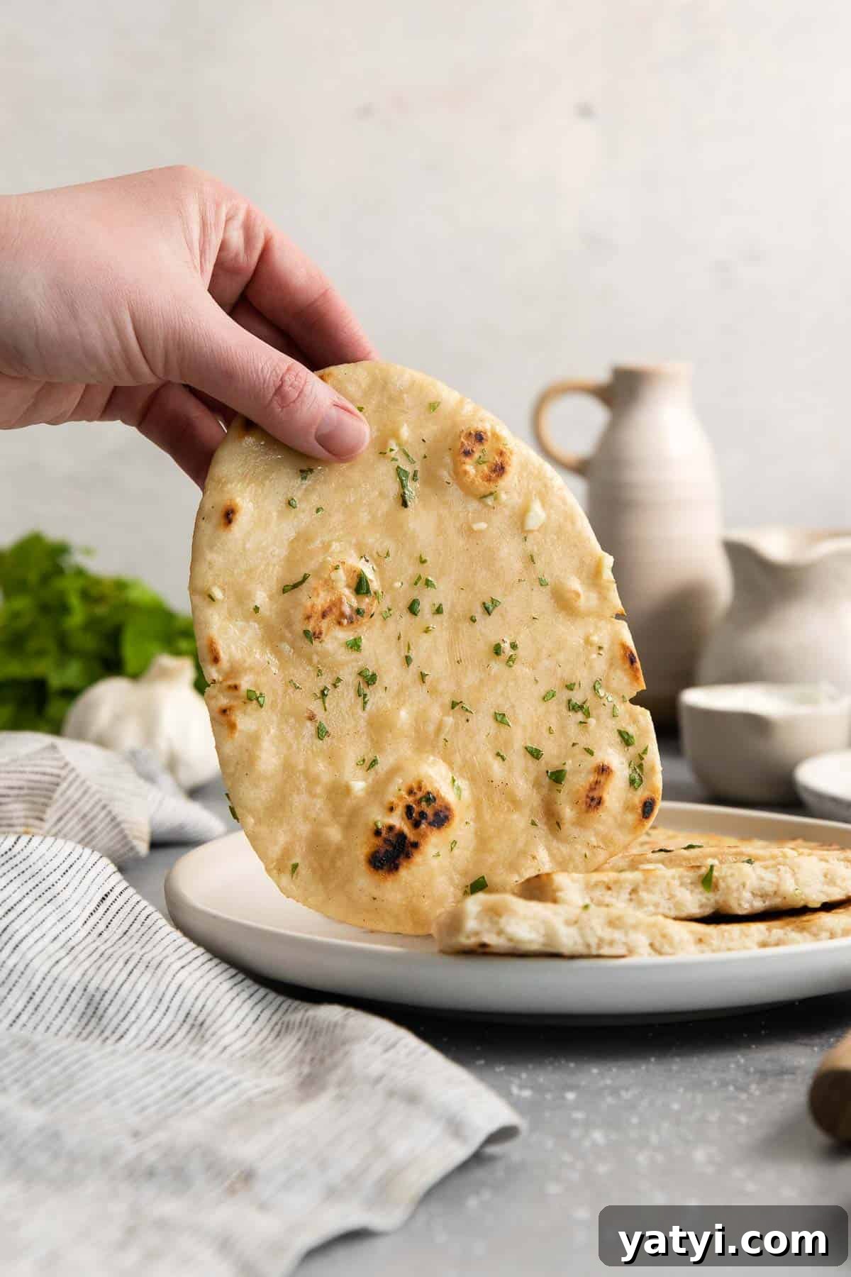 a hand holding up one naan with more laying on the plate.