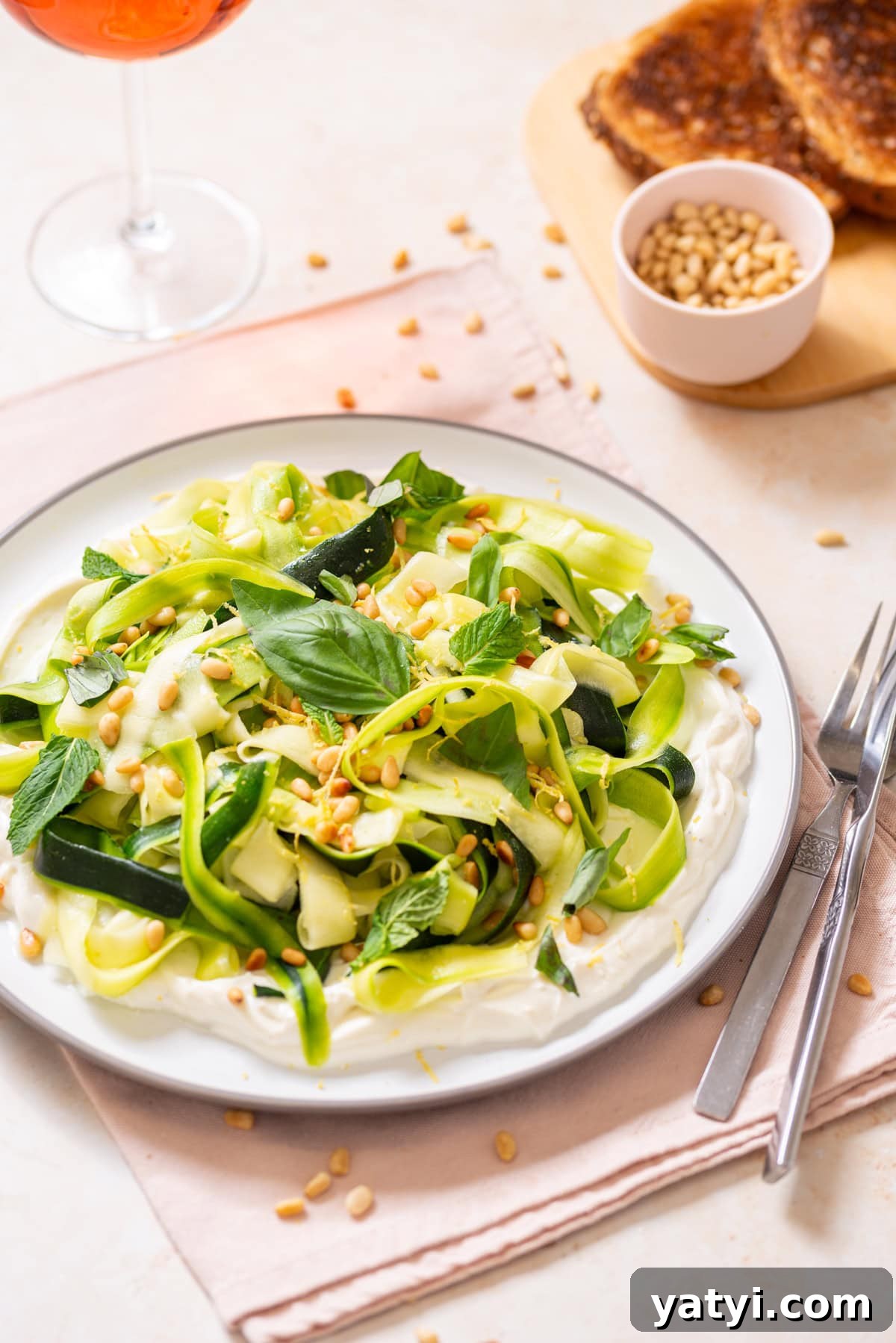 Zucchini Ribbon Salad with Whipped Lemon Ricotta Dressing 2 Zucchini ribbon salad over whipped lemon ricotta topped with basil, mint, toasted pine nuts, olive oil, and lemon zest on a white plate with toast and rosé nearby.