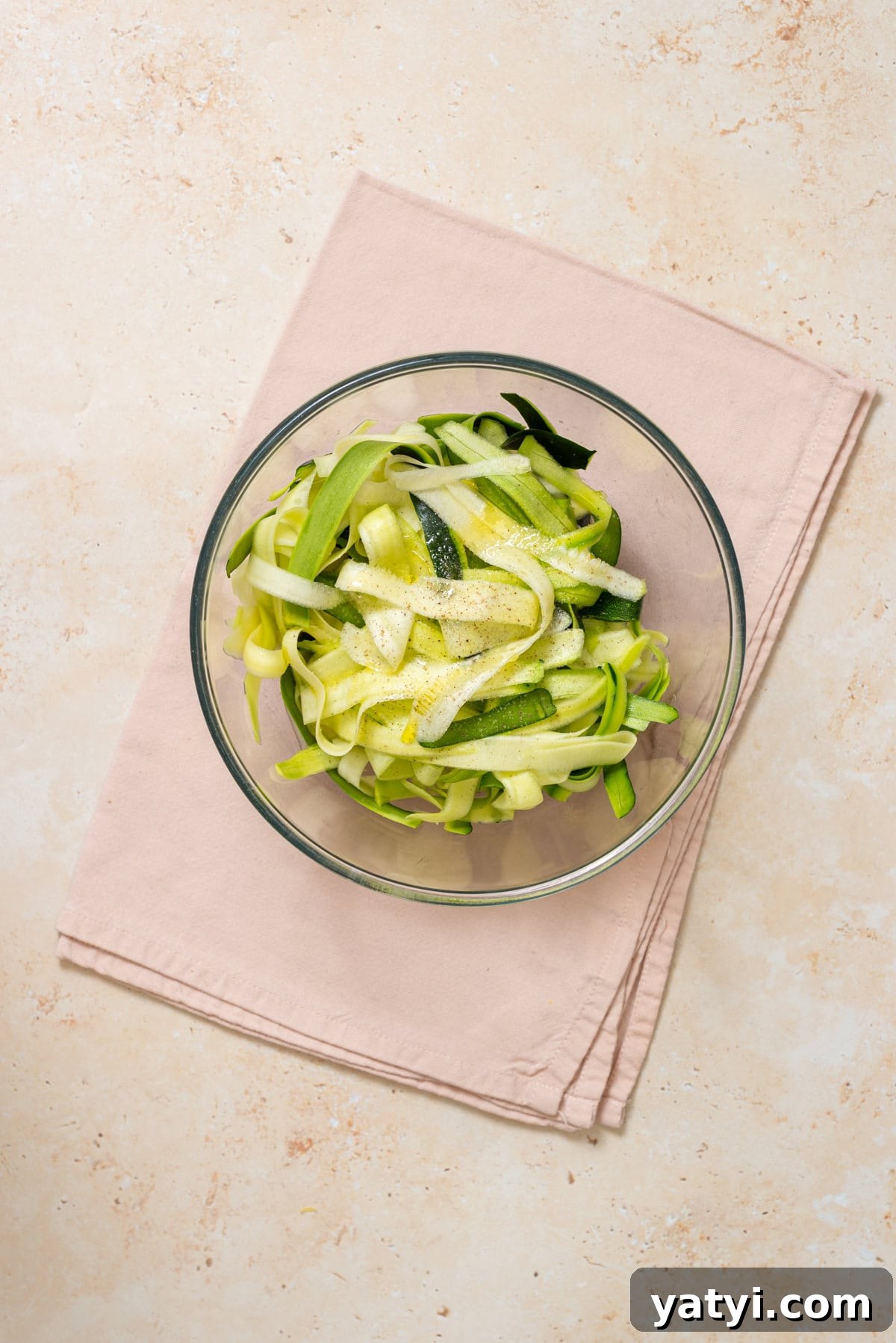 Zucchini Ribbon Salad with Whipped Lemon Ricotta Dressing 9 Fresh zucchini ribbons topped with olive oil, lemon juice, and salt in a glass bowl.