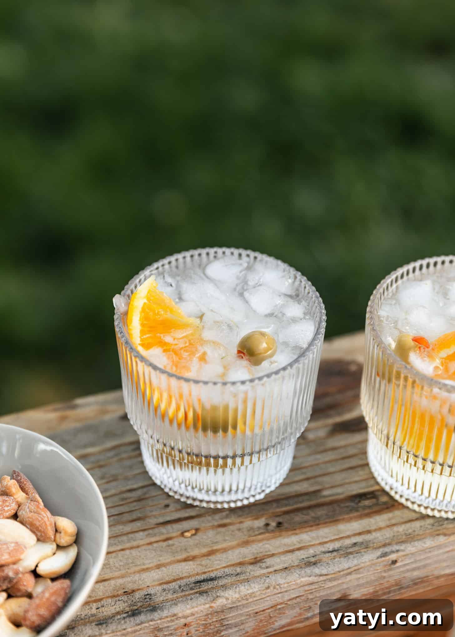 Host an Intimate Dinner Party at Home: Menu, Ambiance & Tips 5 Two spritz cocktails with oranges and olives on a wood board next to a white bowl of nuts at an intimate dinner party.