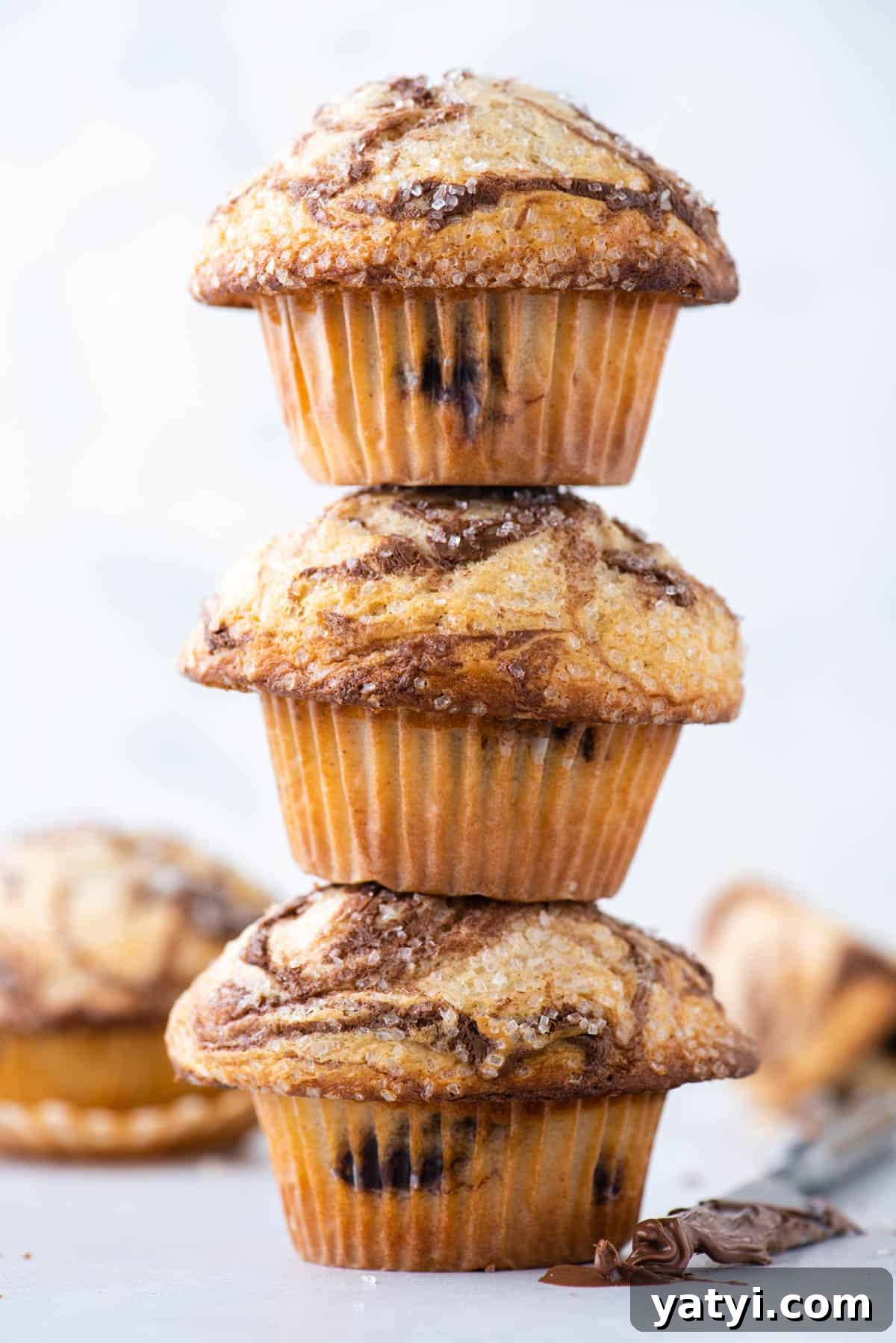 Nutella Swirl Muffins Recipe: Moist Chocolate-Hazelnut Muffins 15 a tower of 3 nutella swirl muffins with more muffins in the background and a butter knife with nutella on it beside the stack