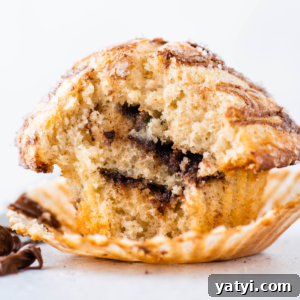 Nutella Swirl Muffins Recipe: Moist Chocolate-Hazelnut Muffins 16 a nutella swirl muffin on a white surface with a white background, with the muffin liner pulled away from the muffin exposing the layers of nutella inside