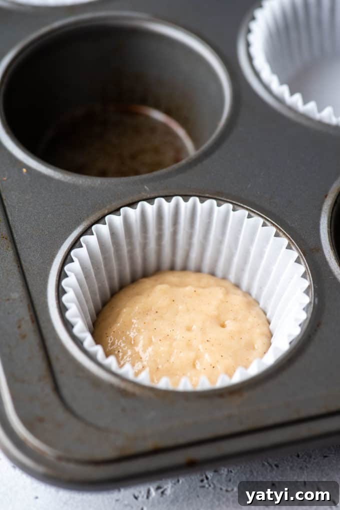 Nutella Swirl Muffins Recipe: Moist Chocolate-Hazelnut Muffins 6 a muffin pan with a white muffin liner in the corner spot and some muffin batter in the bottom of it