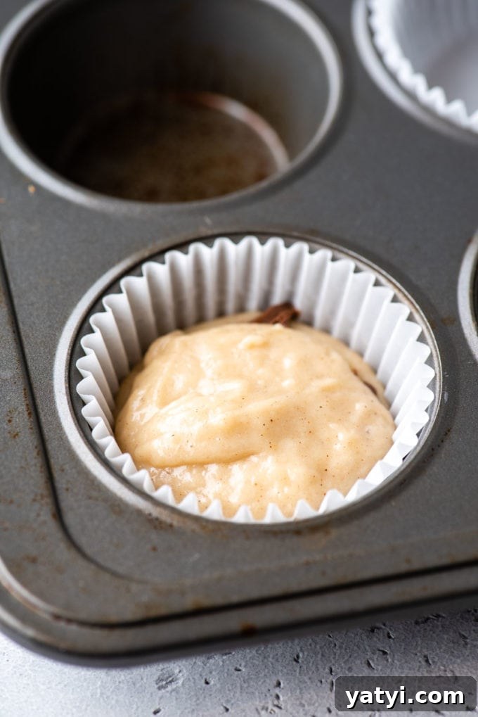 Nutella Swirl Muffins Recipe: Moist Chocolate-Hazelnut Muffins 8 a muffin pan with a white muffin liner in the corner spot and some muffin batter in the bottom of it and layers of muffin batter and nutella inside the liner