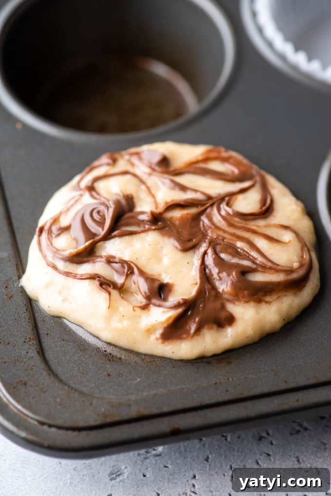 Nutella Swirl Muffins Recipe: Moist Chocolate-Hazelnut Muffins 10 a muffin pan with nutella swirl muffin batter in the corner spot of the pan