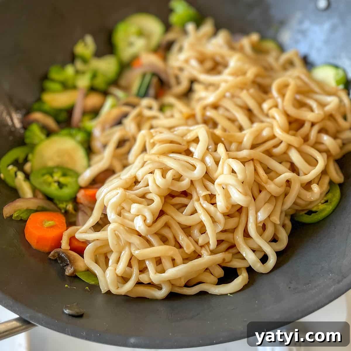 Noodles are added to the wok with vegetables.