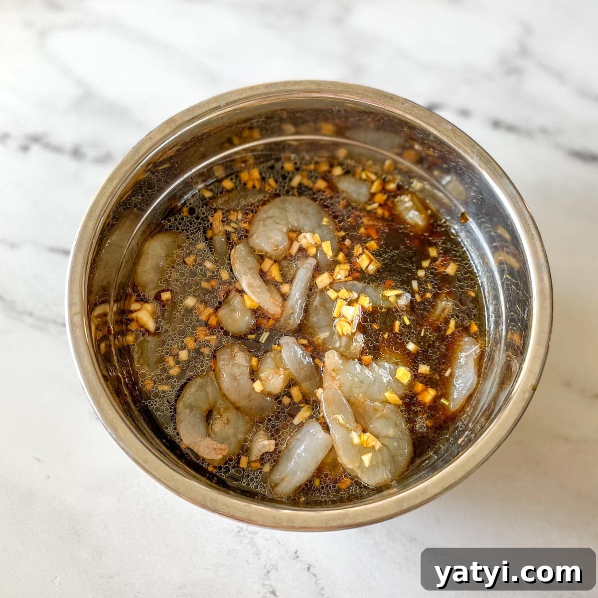 Raw shrimp is shown in a bowl of marinade.