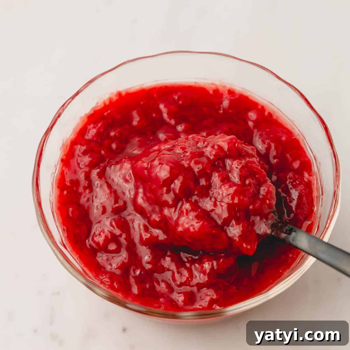 Moist Homemade Strawberry Layer Cake Recipe 5 A bowl of strawberry sauce with a spoon sticking out.