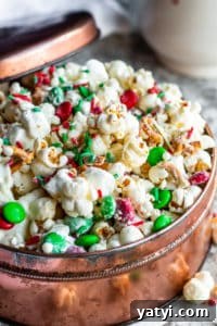 Christmas Crunch Popcorn Snack Mix Christmas Crunch popcorn in a copper tin with lid resting on side on a white counter.