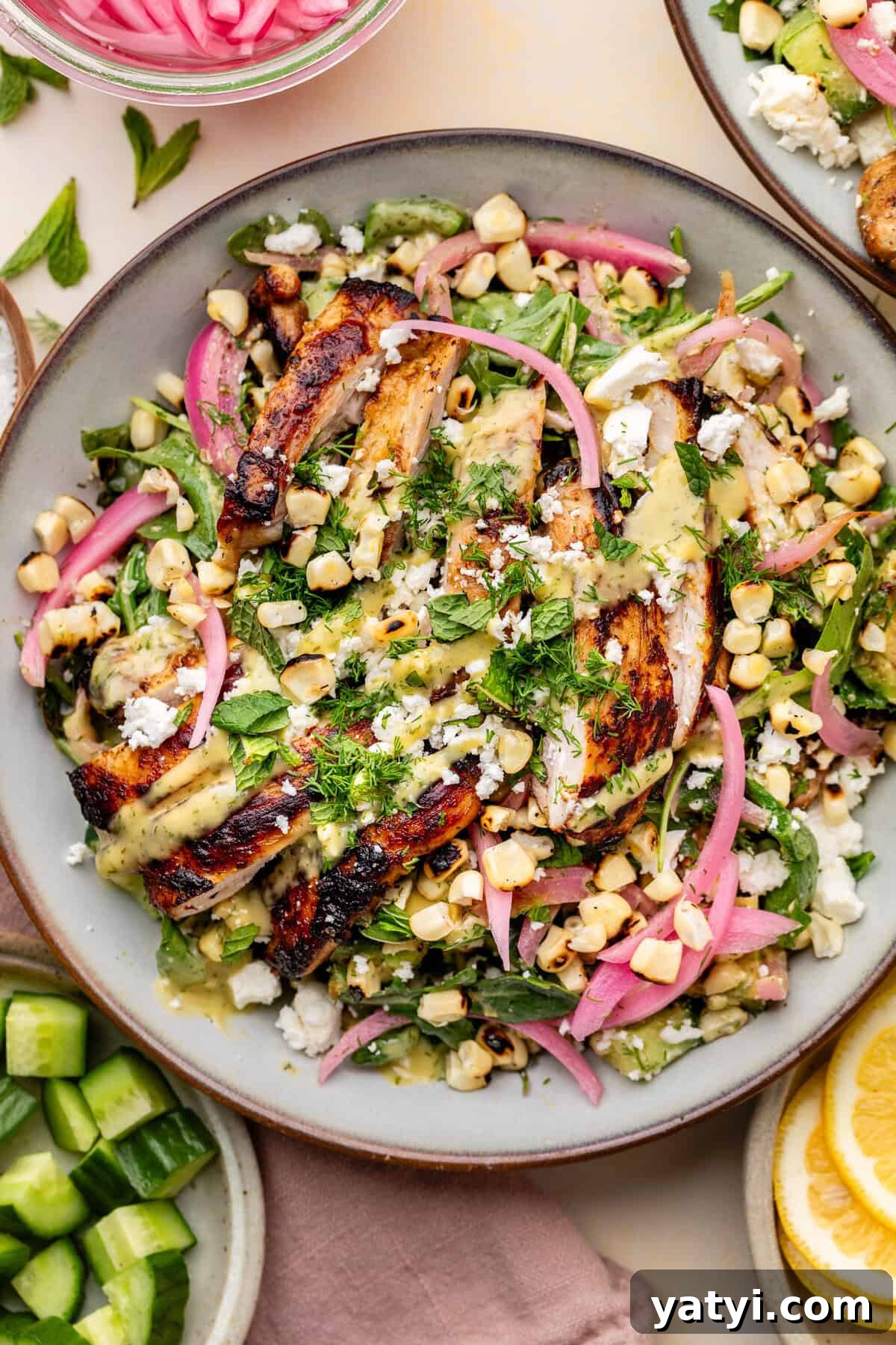 Grilled chicken salad with charred corn, pickled red onions, fresh greens, herbs, and crumbled cheese drizzled with a yellow dressing