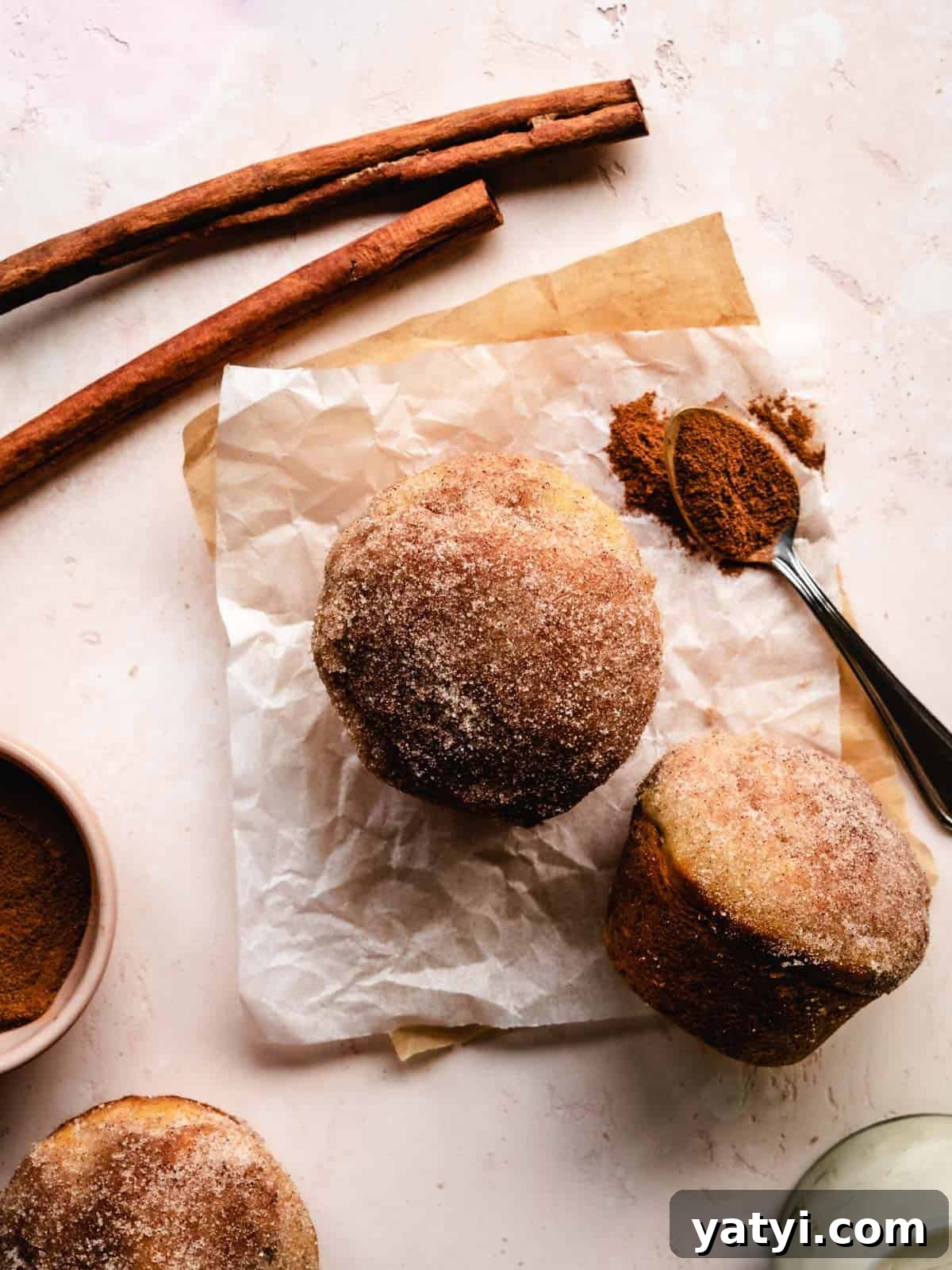 Cinnamon Sugar Donut Muffins Recipe — Soft Baked Donut-Style Muffins 8 donut muffins on parchment paper with cinnamon sticks
