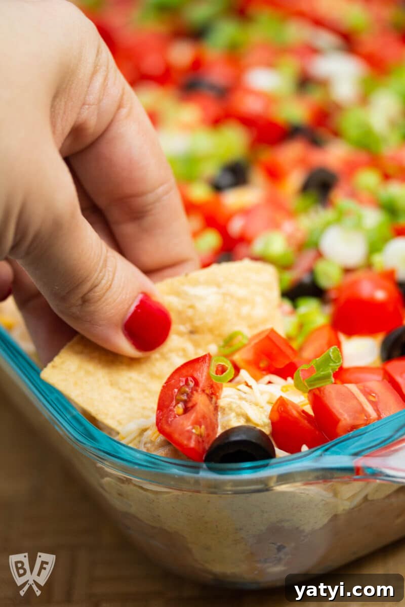 Layered Taco Dip with Refried Beans for Parties and Game Day 11 Dipping a tortilla chip into a layered taco dip.