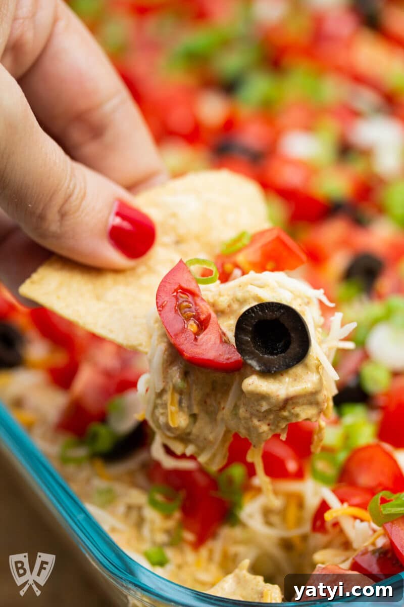 Layered Taco Dip with Refried Beans for Parties and Game Day 12 Scooping layered taco dip onto a tortilla chip.