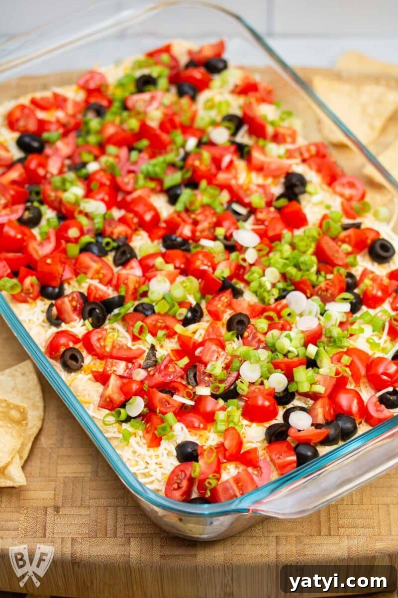 Layered Taco Dip with Refried Beans for Parties and Game Day 13 Serving dish of layered taco dip surrounded by tortilla chips.