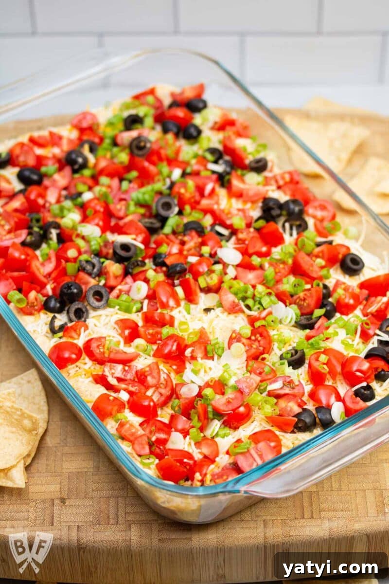 Layered Taco Dip with Refried Beans for Parties and Game Day 14 Tray of layered taco dip with olives removed from one portion.