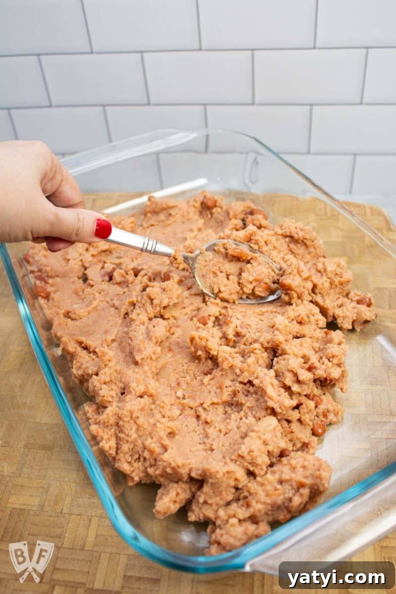 Layered Taco Dip with Refried Beans for Parties and Game Day 5 Spreading refried beans into a serving dish for layered taco dip.