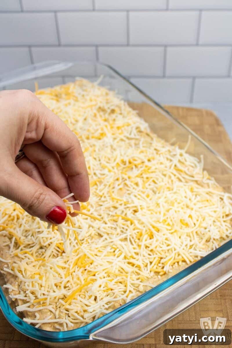 Layered Taco Dip with Refried Beans for Parties and Game Day 7 Sprinkling shredded cheese onto a layered taco dip.