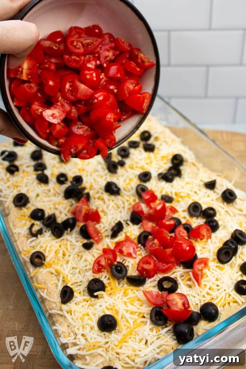 Layered Taco Dip with Refried Beans for Parties and Game Day 9 Adding tomatoes to the top of a layered taco dip.
