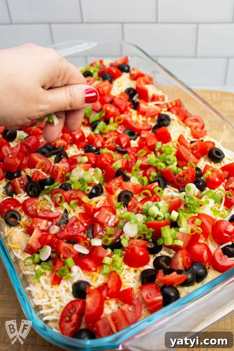 Layered Taco Dip with Refried Beans for Parties and Game Day 10 Scattering green onions on top of a layered taco dip.