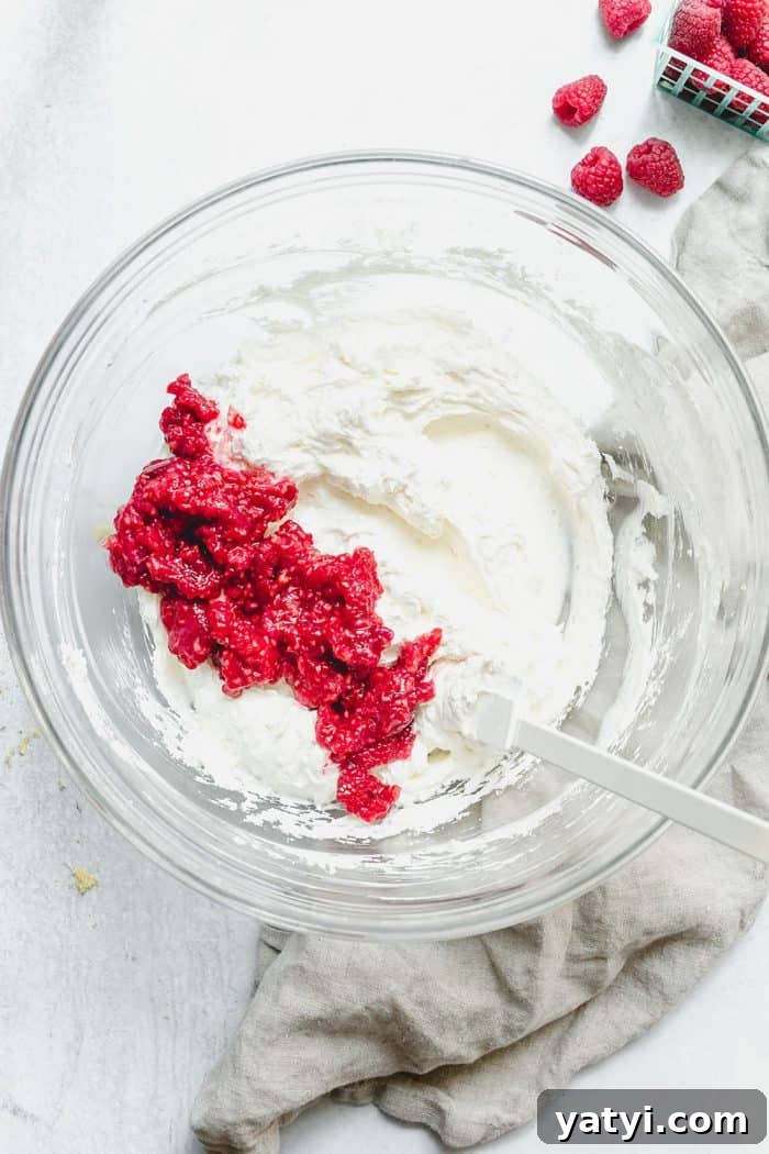 No-Bake Lemon Raspberry Cheesecake Recipe for Fresh Summer Dessert 5 Spatula folding mashed raspberries into the filling for no-bake raspberry lemon cheesecake in a glass mixing bowl