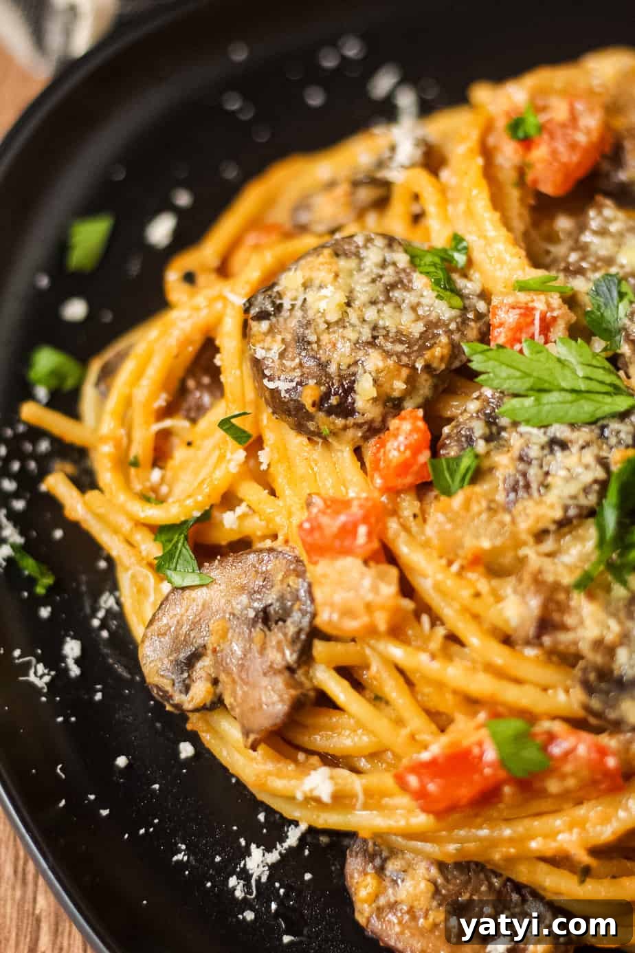 detail shot of creamy cajun mushroom pasta on a black plate on wooden surface.