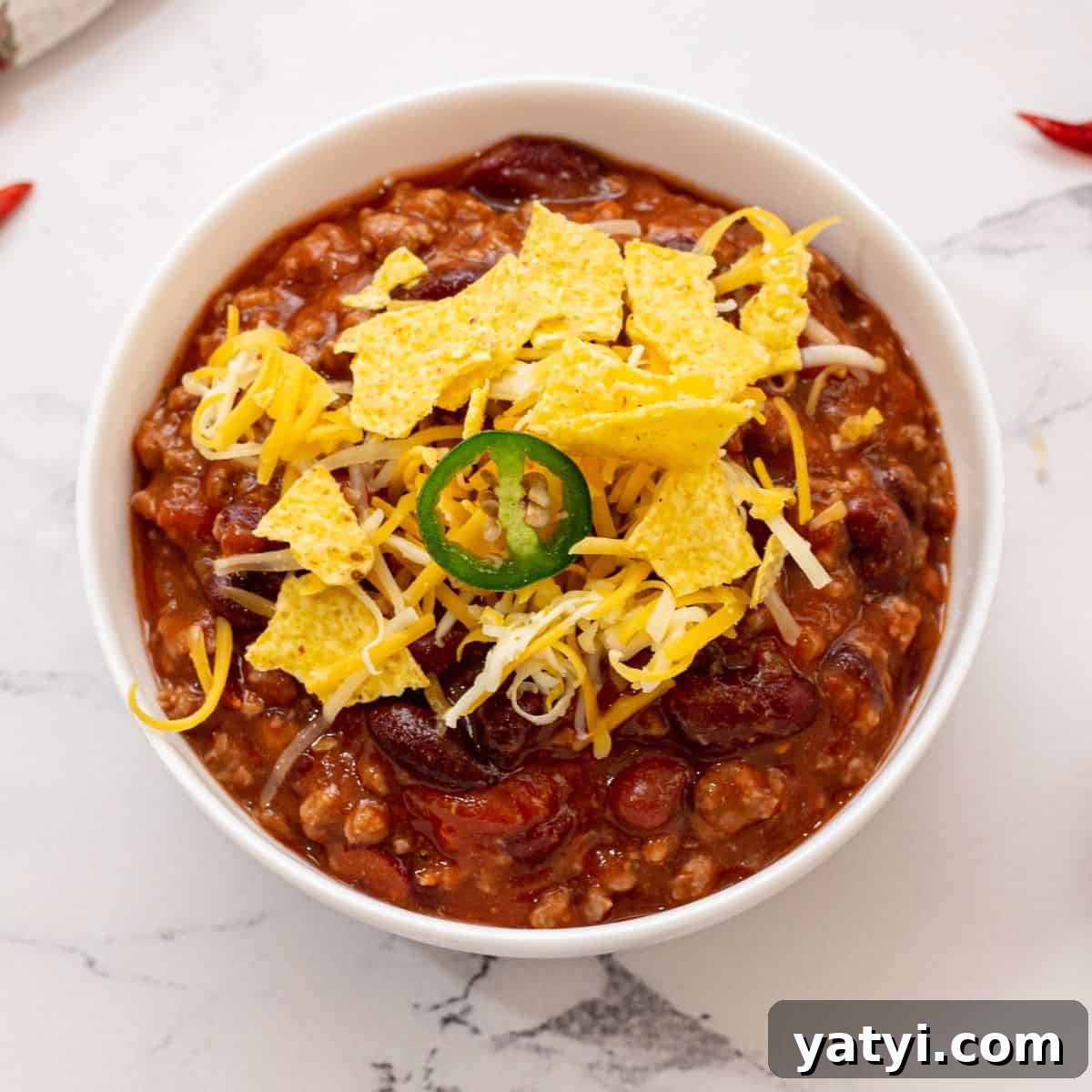 Best Chili Recipes Bowl of crockpot chili topped with corn chips, shredded cheese, and jalapeno.