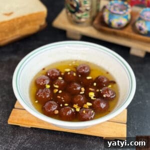 Instant Bread Gulab Jamun Recipe — Soft, No-Yeast Indian Dessert 5 Gulab Jamun with bread in syrup, garnished with chopped nuts, served in a white bowl.