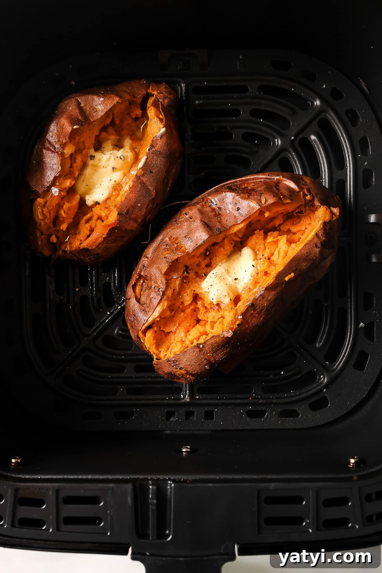 Crispy Air Fryer Sweet Potatoes: Quick Roast in 20 Minutes 8 Two sweet potatoes cut open and topped with butter in an air fryer basket.